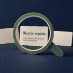 A green paper magnifying glass frames a card labelled Bicycle repairs against a navy background.