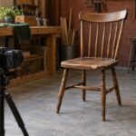 A camera on a tripod points at a chipped wooden chair, ready to take a photo for a repair enquiry.